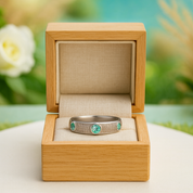 Silver ring with green gemstones in a wooden box against a blurred natural background