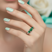 Silver ring with three green gemstones on a light background