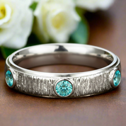 Silver ring with turquoise gemstones on a wooden surface with blurred flowers in the background