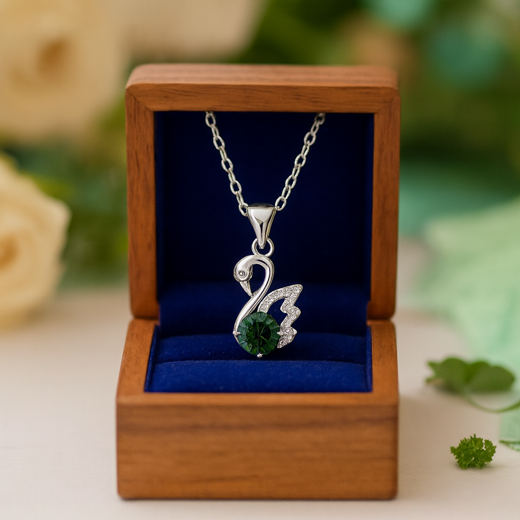 Silver swan pendant necklace with green gemstone in a wooden box on a blurred natural background