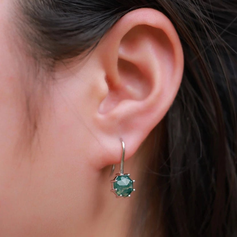 Close-up of an ear wearing a green gemstone earring with dark hair in the background