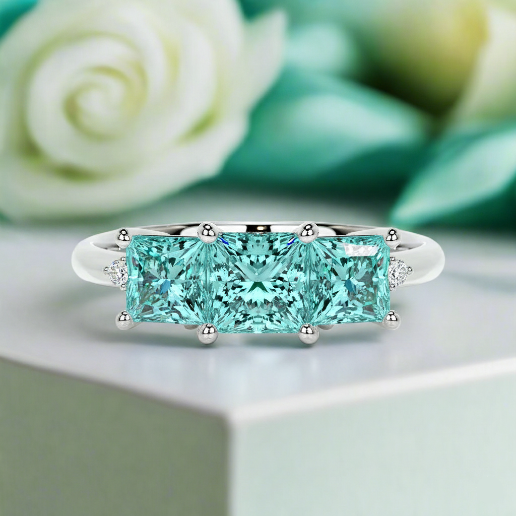Teal diamond ring on a white surface with a blurred green background