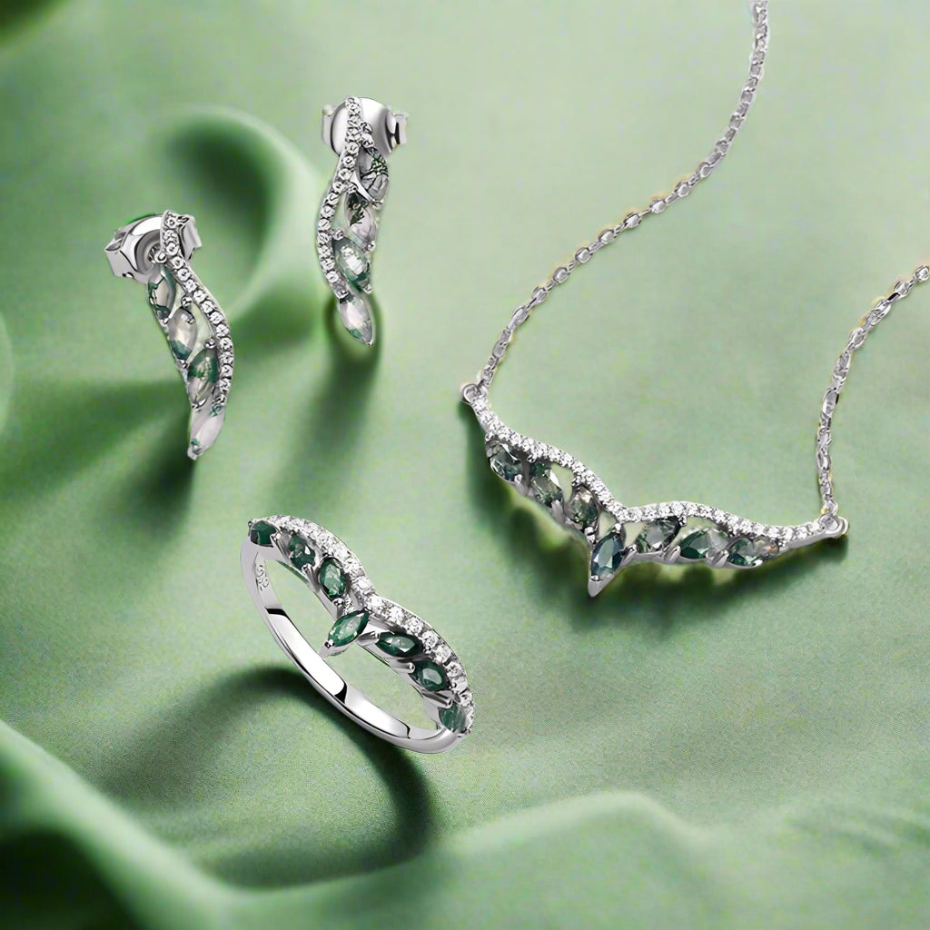 Silver jewelry set with green gemstones including necklace, earrings, and ring on a light gray background.
