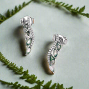 Pair of silver earrings with green gemstones on a light gray background
