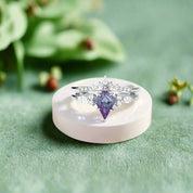 Two rings with purple gemstones on a white dish with flowers and pearls.