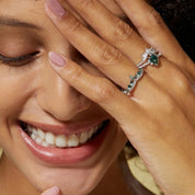 Woman wearing a ring with emerald and diamonds, smiling.