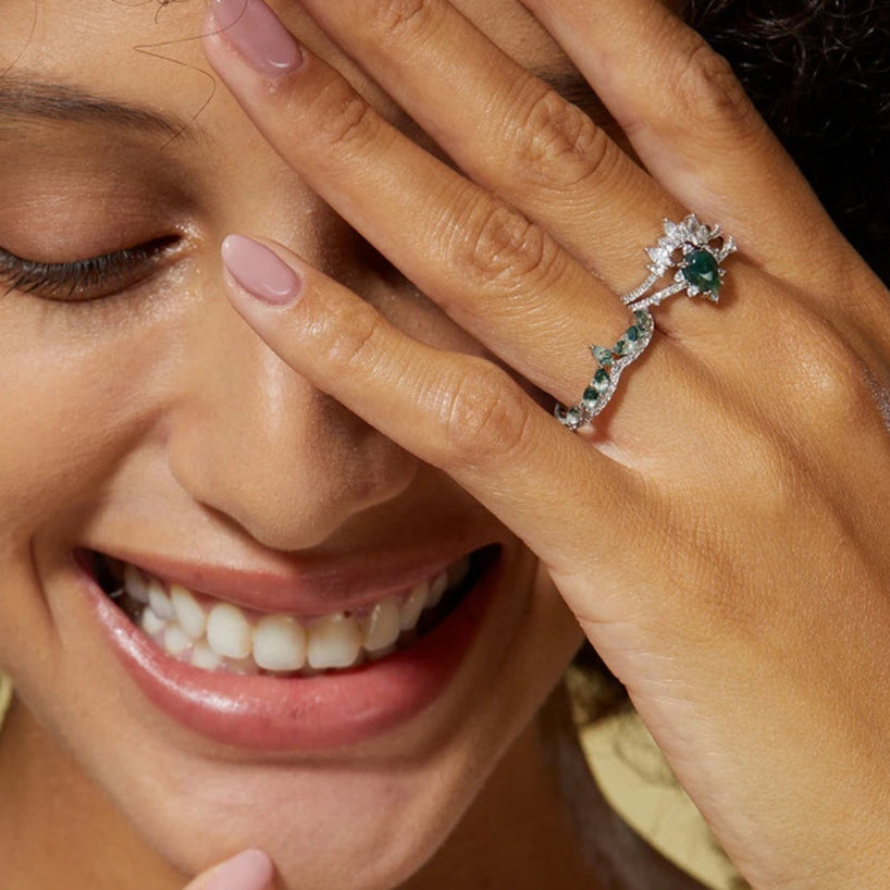 Woman wearing a ring with emerald and diamonds, smiling.