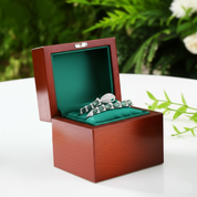 Wooden jewelry box with a ring inside on a white surface with greenery in the background