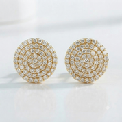A pair of round gold stud earrings covered in concentric rings of clear pavé gemstones, displayed on a clean white reflective surface.