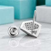 A close-up product shot of a silver-toned jewelry finding, showing a faceted geometric backplate with a threaded screw post and a separate matching screw-back piece on a light marble surface.