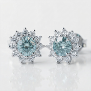 A pair of silver-toned halo stud earrings featuring round light blue gemstones surrounded by clear accent stones, shown on a clean white background.