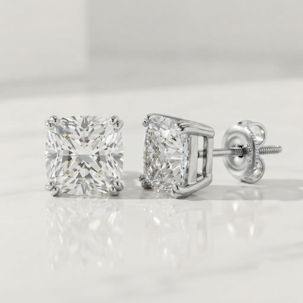A pair of princess-cut diamond stud earrings in a silver-colored four-prong setting, shown on a reflective white surface with a soft gray background.