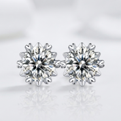 A pair of round brilliant-cut diamond stud earrings in a snowflake or starburst cluster setting, shown on a clean white reflective surface.