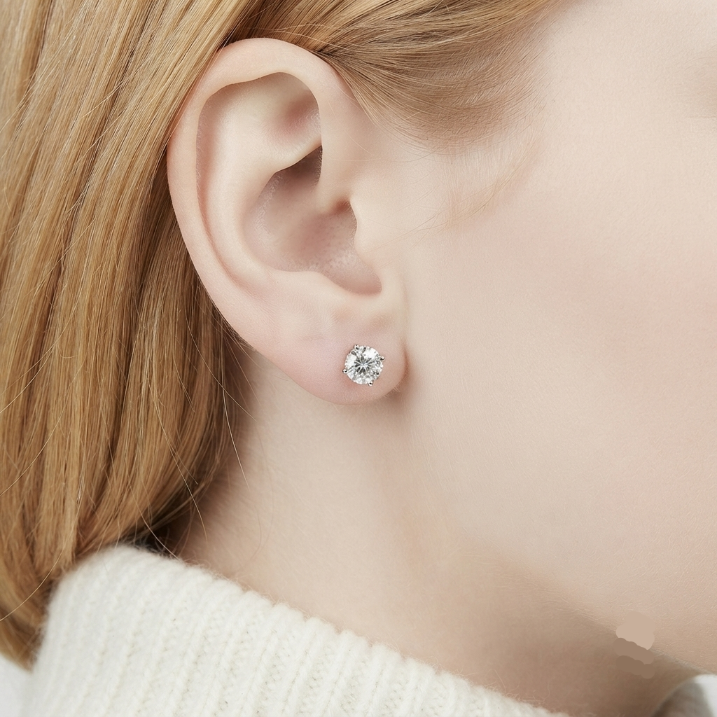 A close-up of a person's ear wearing a small round clear stud earring, with light blonde hair and a white ribbed sweater visible.