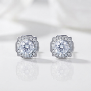 A pair of silver-toned stud earrings with large round clear center stones and smaller surrounding stones, shown on a clean white reflective surface.