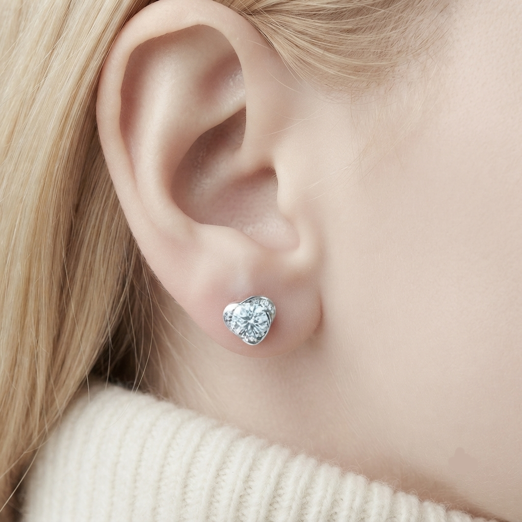 A close-up of a person's ear wearing a small heart-shaped stud earring with a silver-toned setting and clear stones.