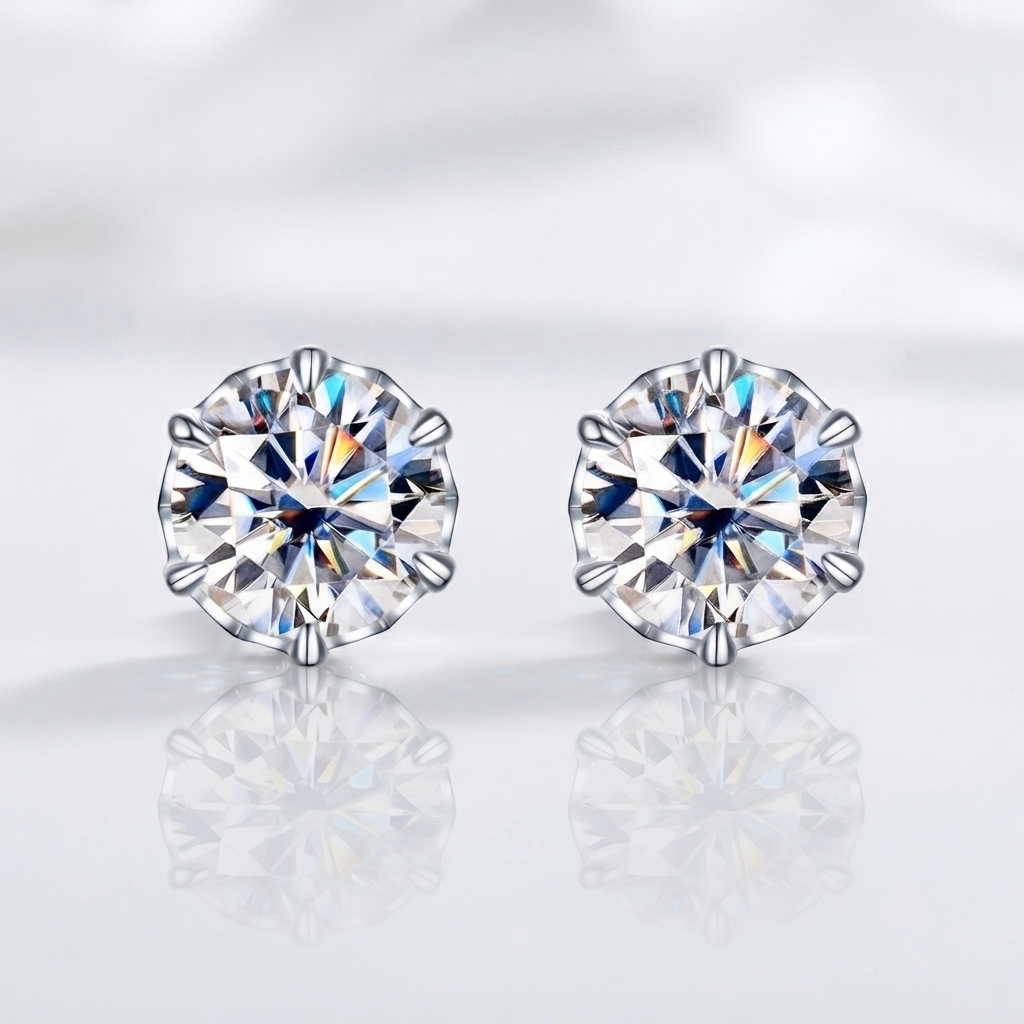 A pair of round-cut stud earrings with sparkling clear gemstones in silver-toned prong settings, displayed on a soft white reflective surface.