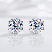 A pair of round-cut stud earrings with sparkling clear gemstones in silver-toned prong settings, displayed on a soft white reflective surface.