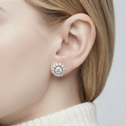 A close-up of a model's ear wearing a round halo stud earring with a silver-toned metal setting and clear stones.
