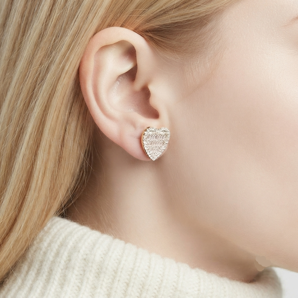 A close-up of a model's ear wearing a small heart-shaped stud earring covered in clear crystals on a silver-tone base.