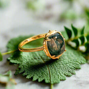 Gold ring with a green gemstone on a wooden surface with a blurred green plant background